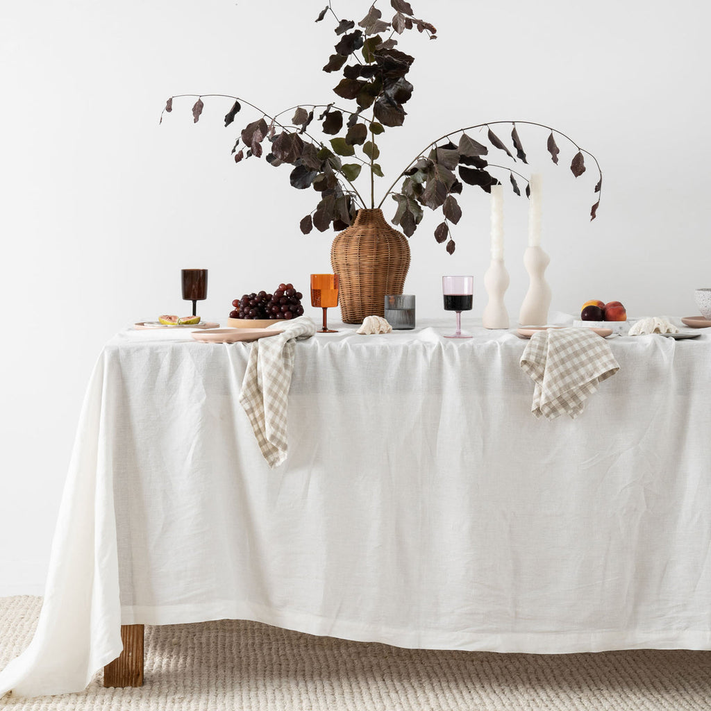 Elegant table setting with a white tablecloth, decorative vase, and candles on a plain background