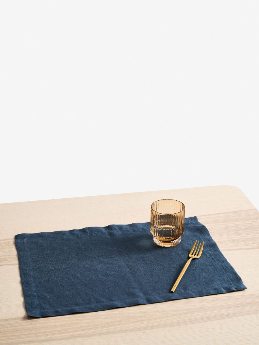 Navy blue placemat with a glass and fork on a wooden table
