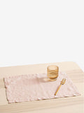 Pink textured napkin on a wooden table with a gold fork and glass.