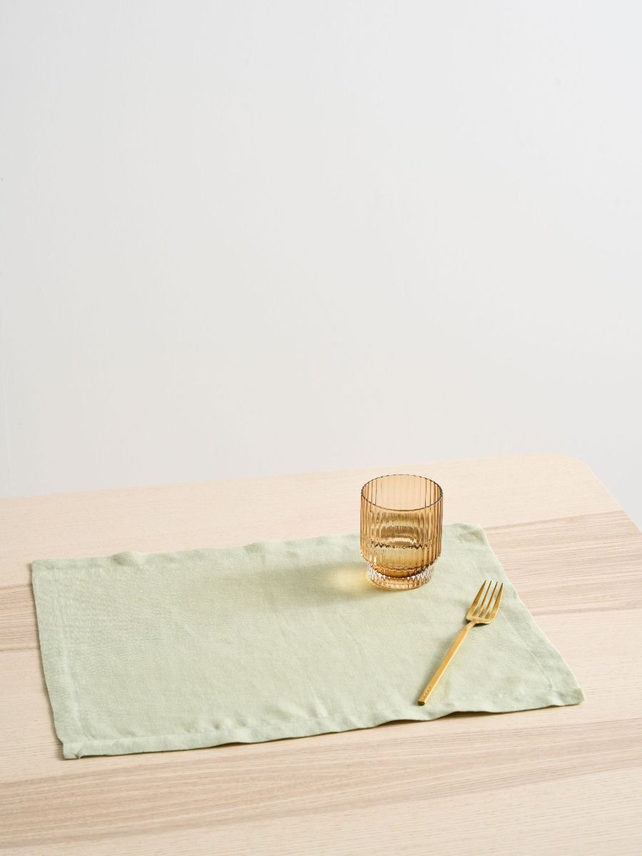 Sage green placemat with a gold fork and woven glass on a wooden table.