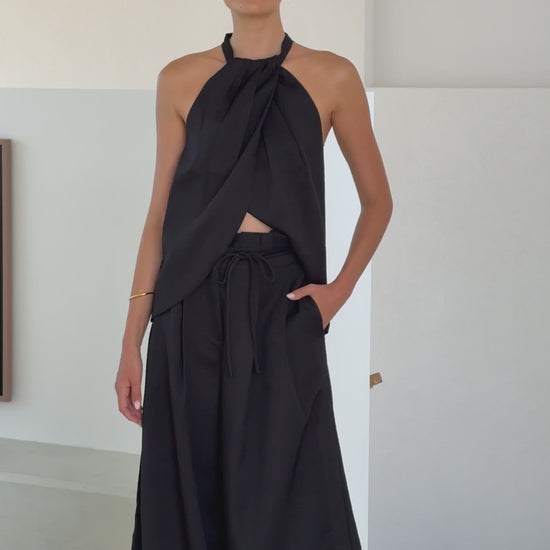 Model wearing black crepe halter top with draped neckline and open back

