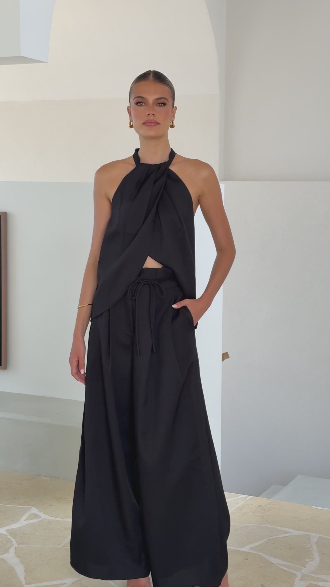 Model wearing black crepe halter top with draped neckline and open back

