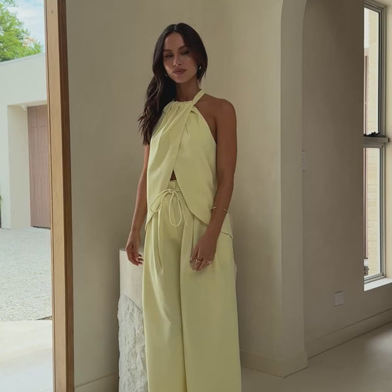 Model wearing butter yellow crepe halter top with front drape and open back
