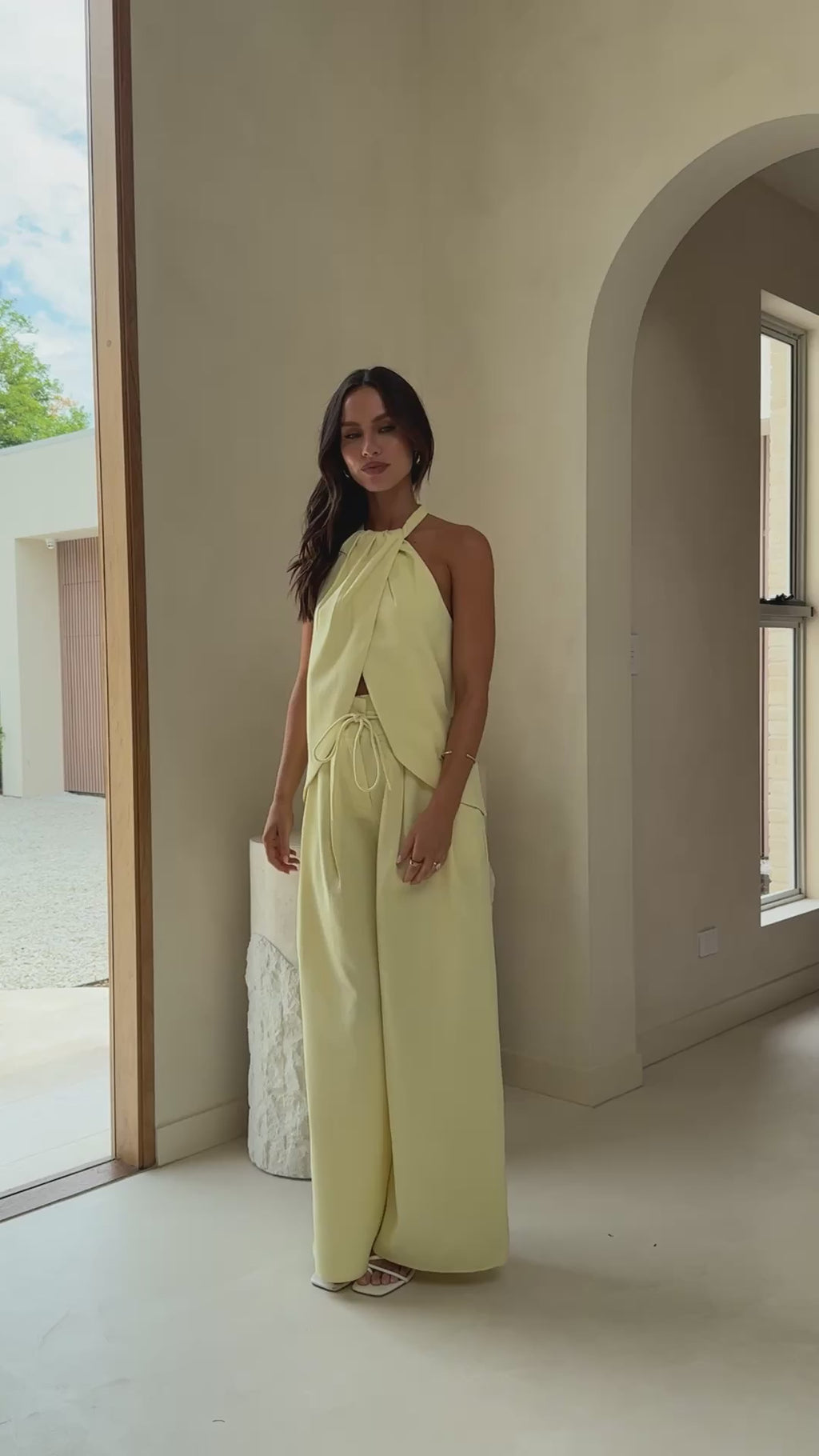 Model wearing butter yellow crepe halter top with front drape and open back