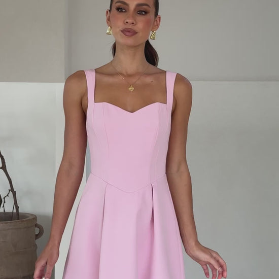 A model wearing a baby pink mini dress made of banana crepe fabric with a sweetheart neckline and a full skirt.