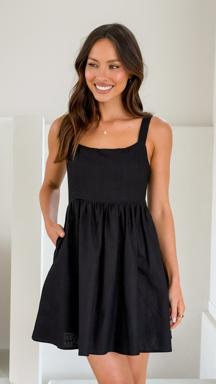 Black linen mini dress with square neckline, sleeveless straps, and smocked back