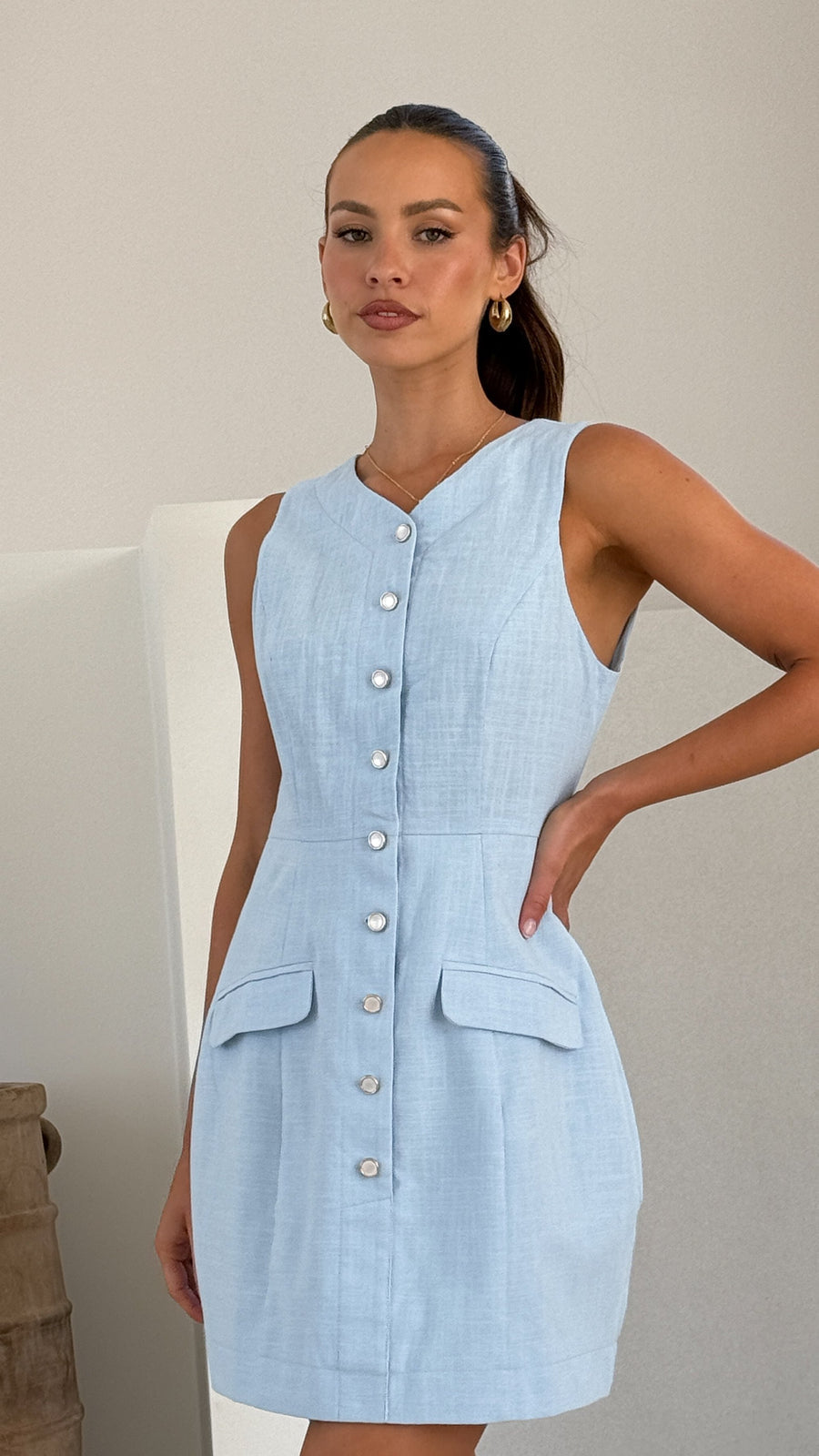 Powder blue linen mini dress with sleeveless cut, front buttons, and flap pockets