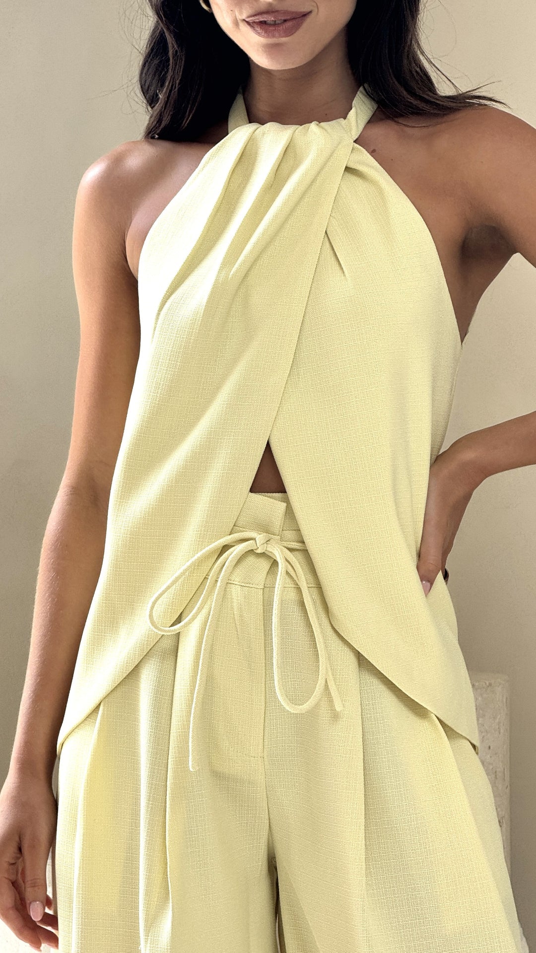 Model wearing butter yellow crepe halter top with front drape and open back